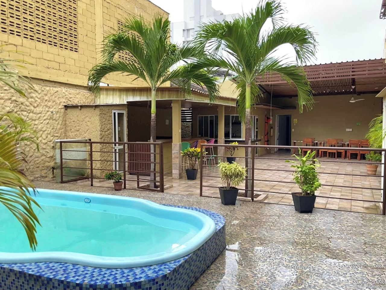 A swimming pool with a tiled edge, surrounded by potted plants and a covered outdoor seating area.