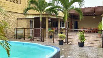 A swimming pool with a tiled edge, surrounded by potted plants and a covered outdoor seating area.