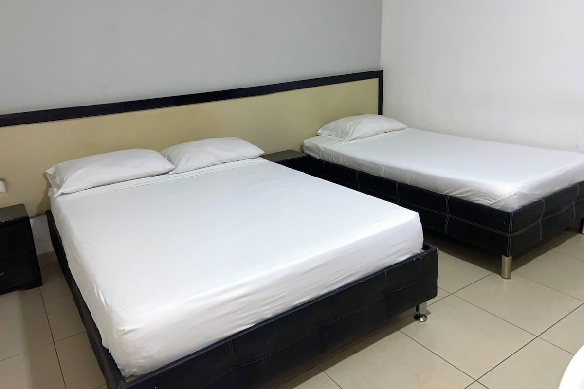 A hotel room with two beds, a nightstand, and a wall-mounted light fixture.