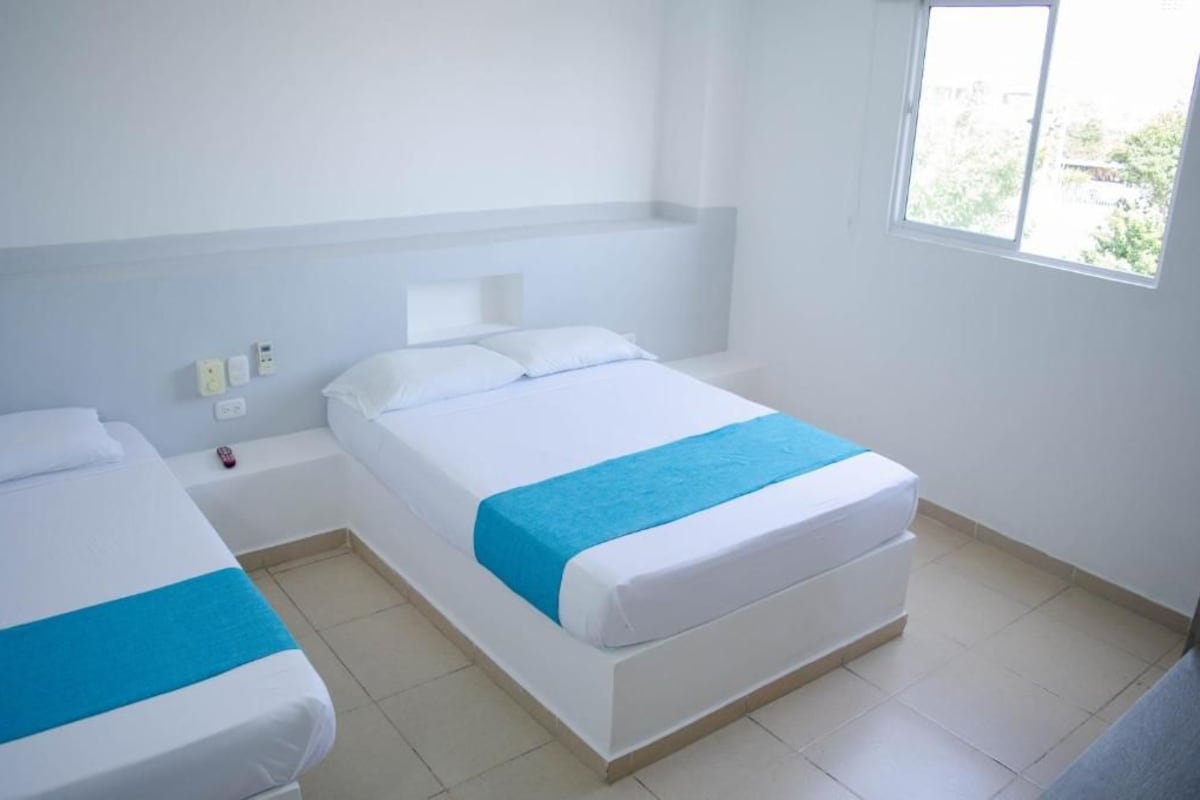 A hotel room with two beds, a window, and a bedside table.