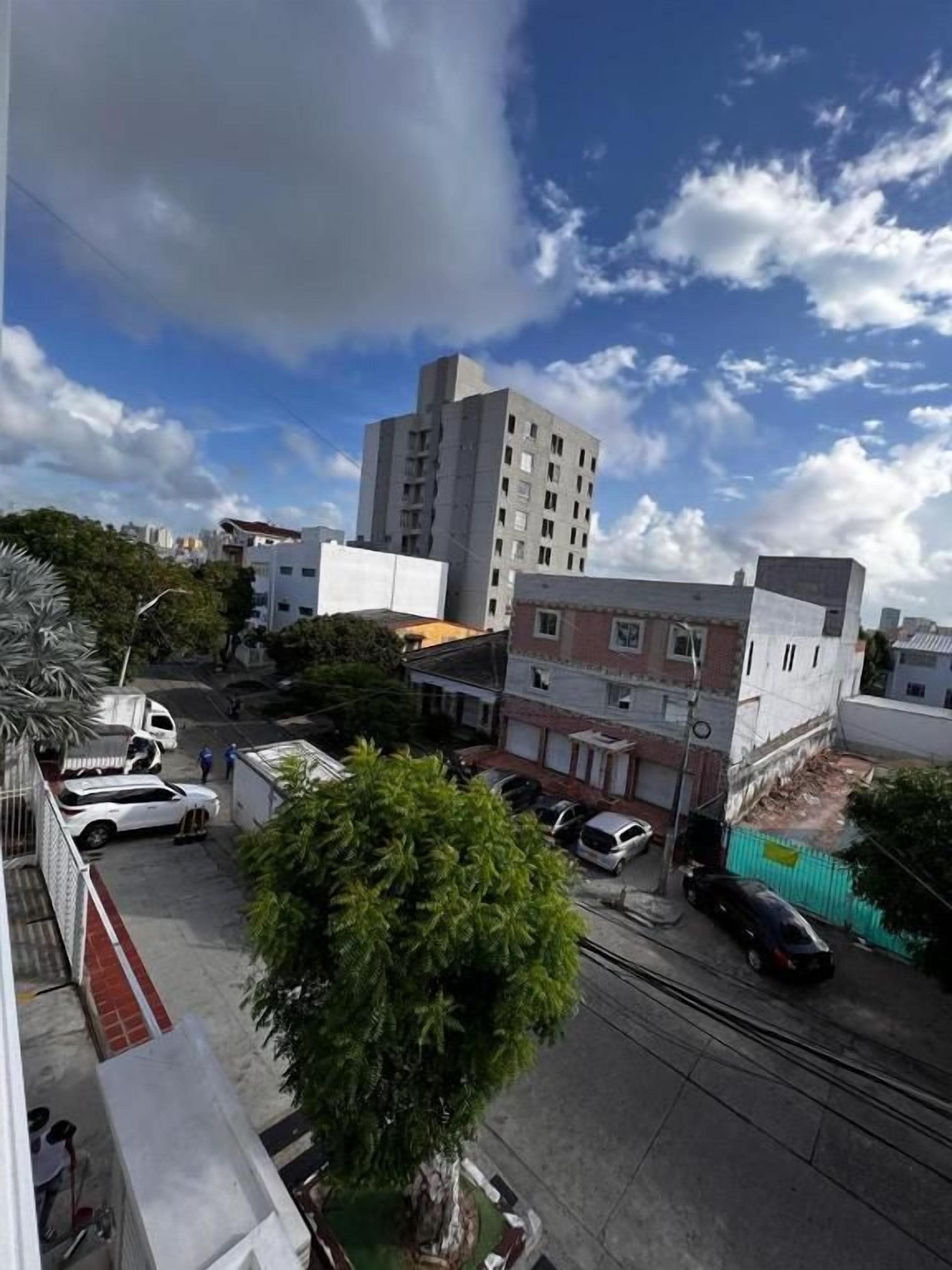 Vista de una calle con edificios, un árbol y coches estacionados.