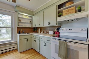 Una cocina con armarios blancos, una estufa blanca y un ventanal con vistas a árboles.