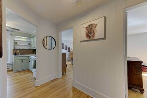 Un couloir avec un plancher en bois, un coin cuisine avec un évier et des placards, un miroir et un tableau représentant un animal accroché au mur.