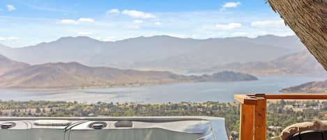 A hot tub with a mountain view, a wooden deck, and a clear sky.