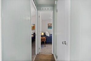 Ein Flur, der in ein Schlafzimmer mit einem Bett, einem Nachttisch und einem Bild an der Wand führt.
