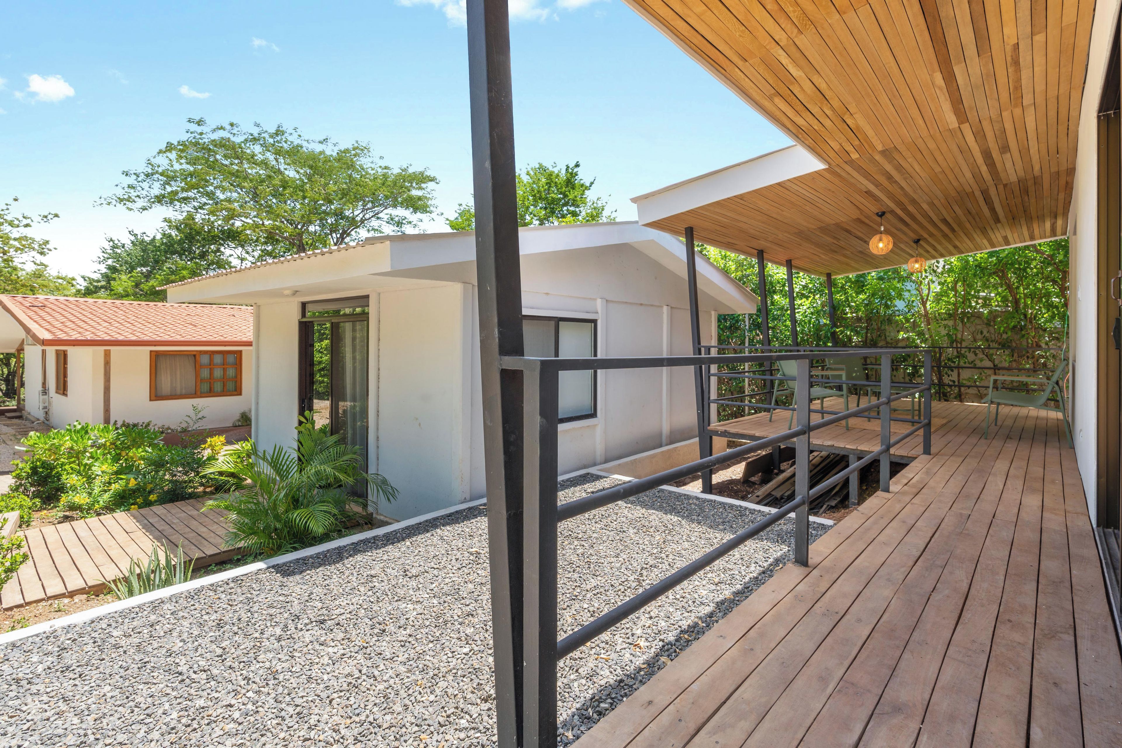 Une terrasse en bois avec une rambarde, un petit bâtiment à la façade blanche et un ciel dégagé.
