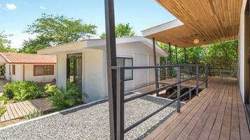 Une terrasse en bois avec une rambarde, un petit bâtiment à la façade blanche et un ciel dégagé.