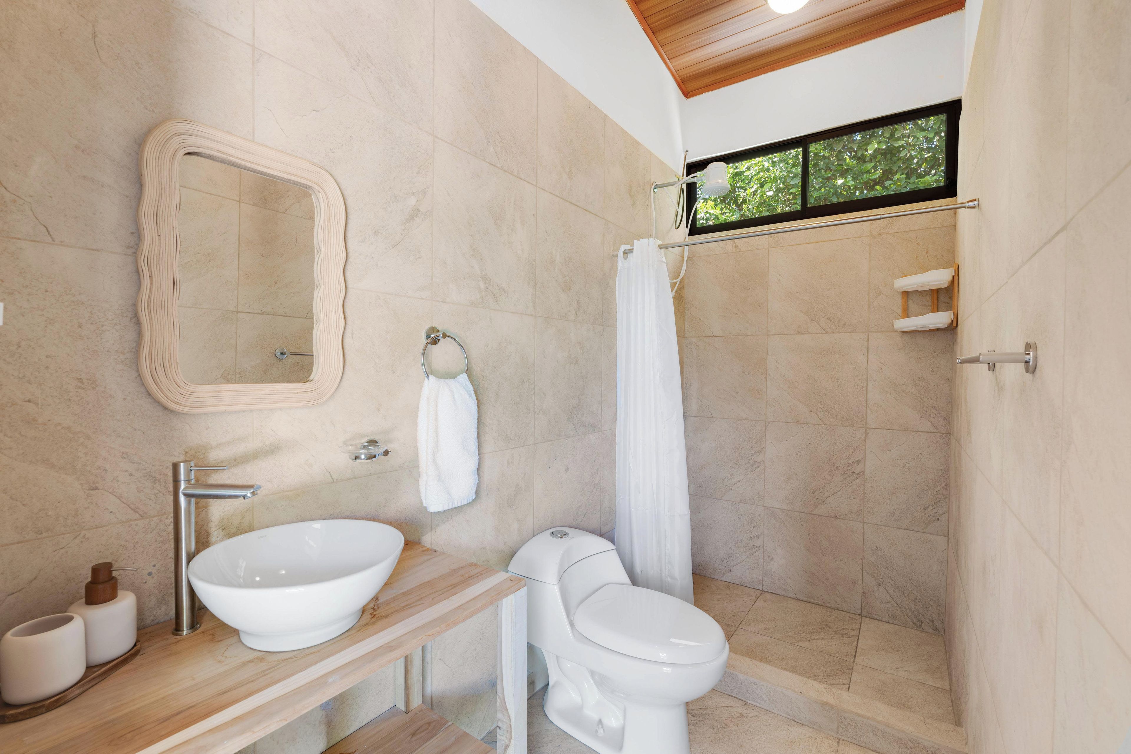 Une salle de bain avec un grand miroir, un lavabo, des toilettes et un espace douche.