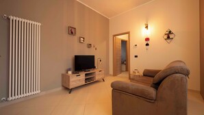 Sala de estar con sofá, televisión y radiador. Hay una puerta que da a otra habitación.