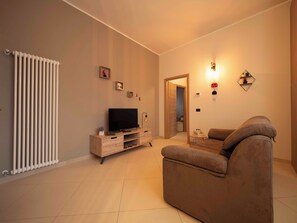 Een woonkamer met een bank, televisie en een radiator. Er is een deur die naar een andere kamer leidt.