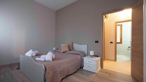 Un dormitorio con cama, mesitas de noche y un baño visible a través de una puerta abierta.