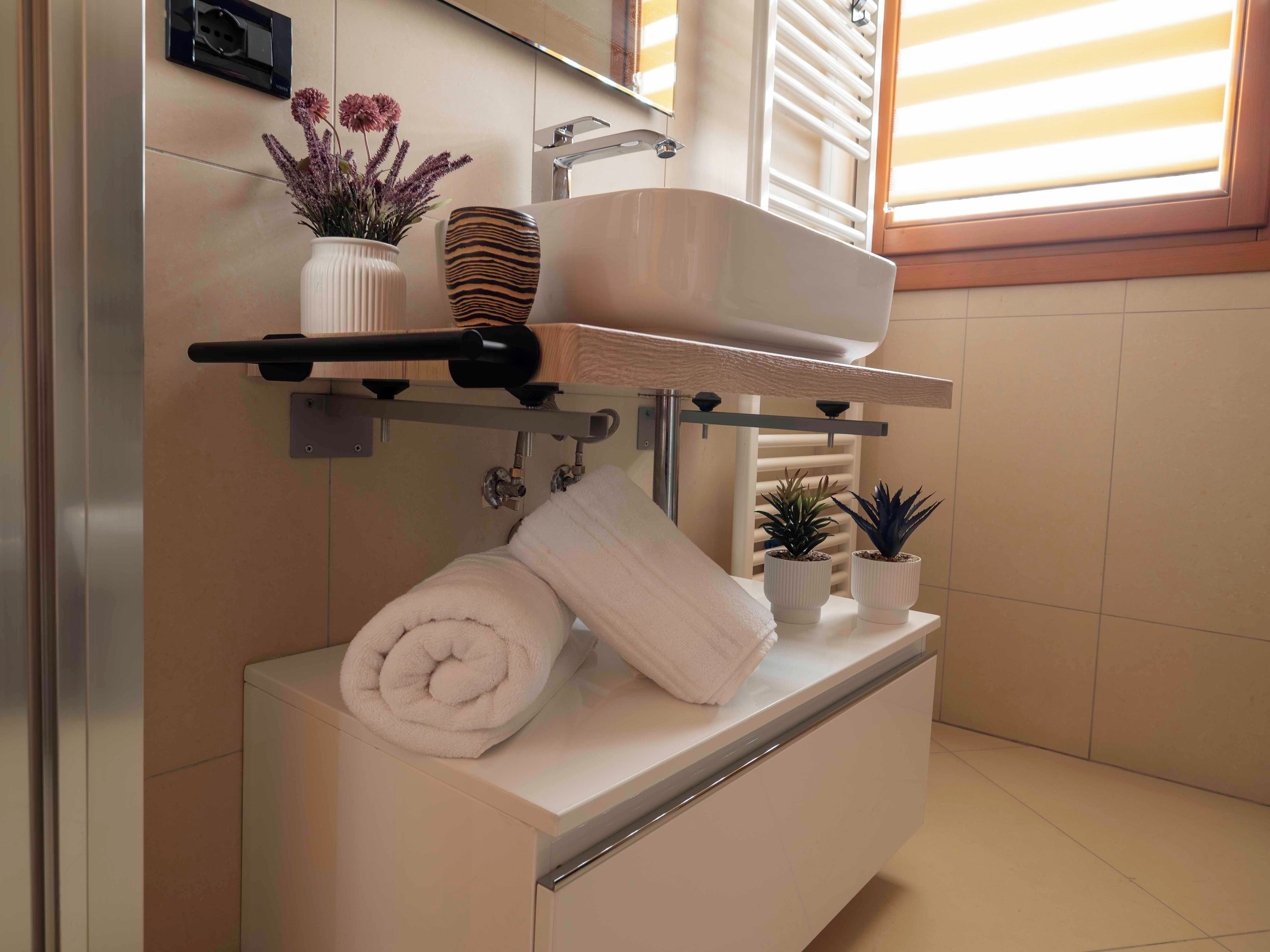 Casa de banho com lavatório branco, suporte de toalhas e duas plantas em vasos.