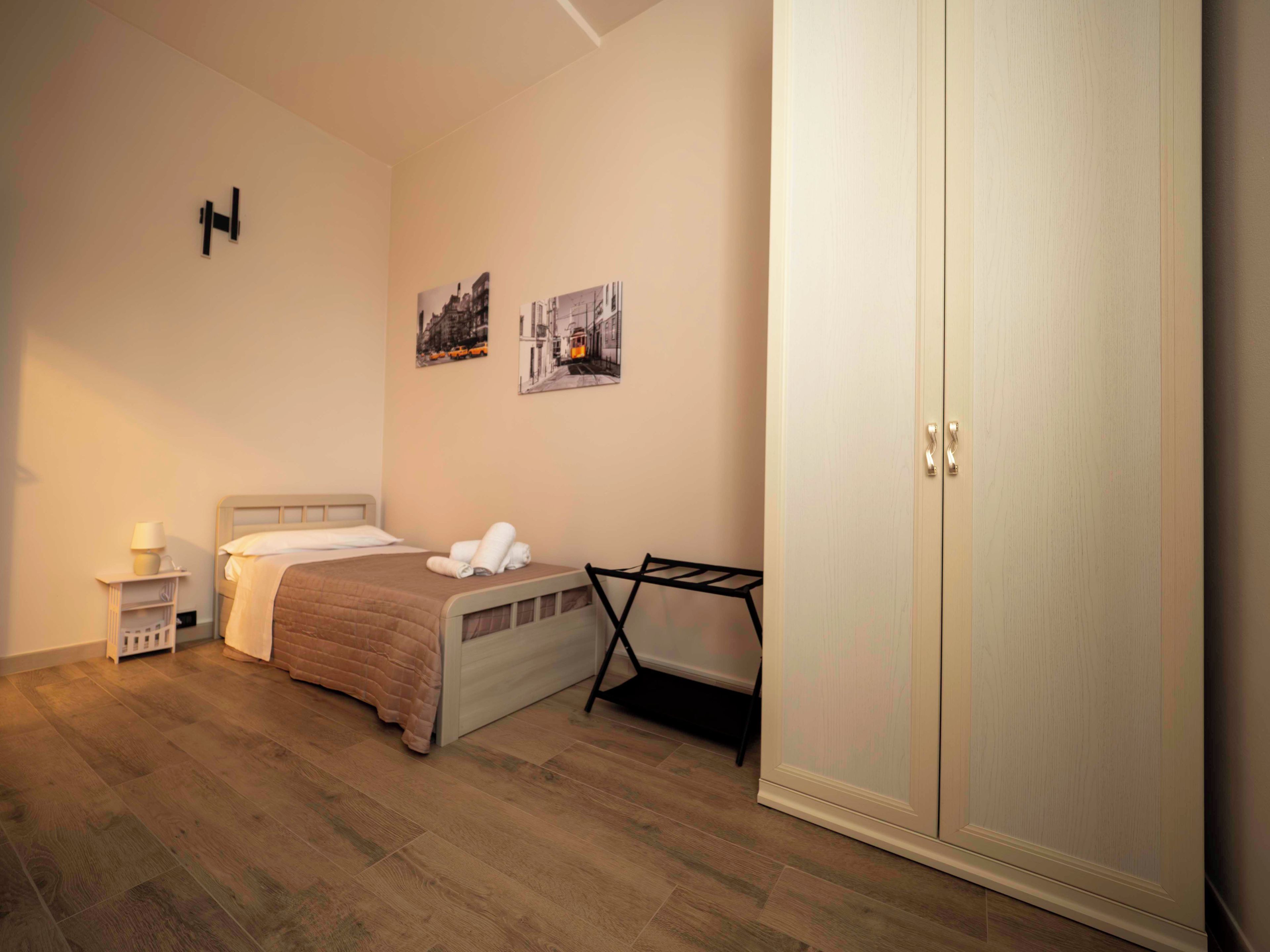 A bedroom with a bed, a nightstand, a wardrobe, and two wall-mounted pictures.