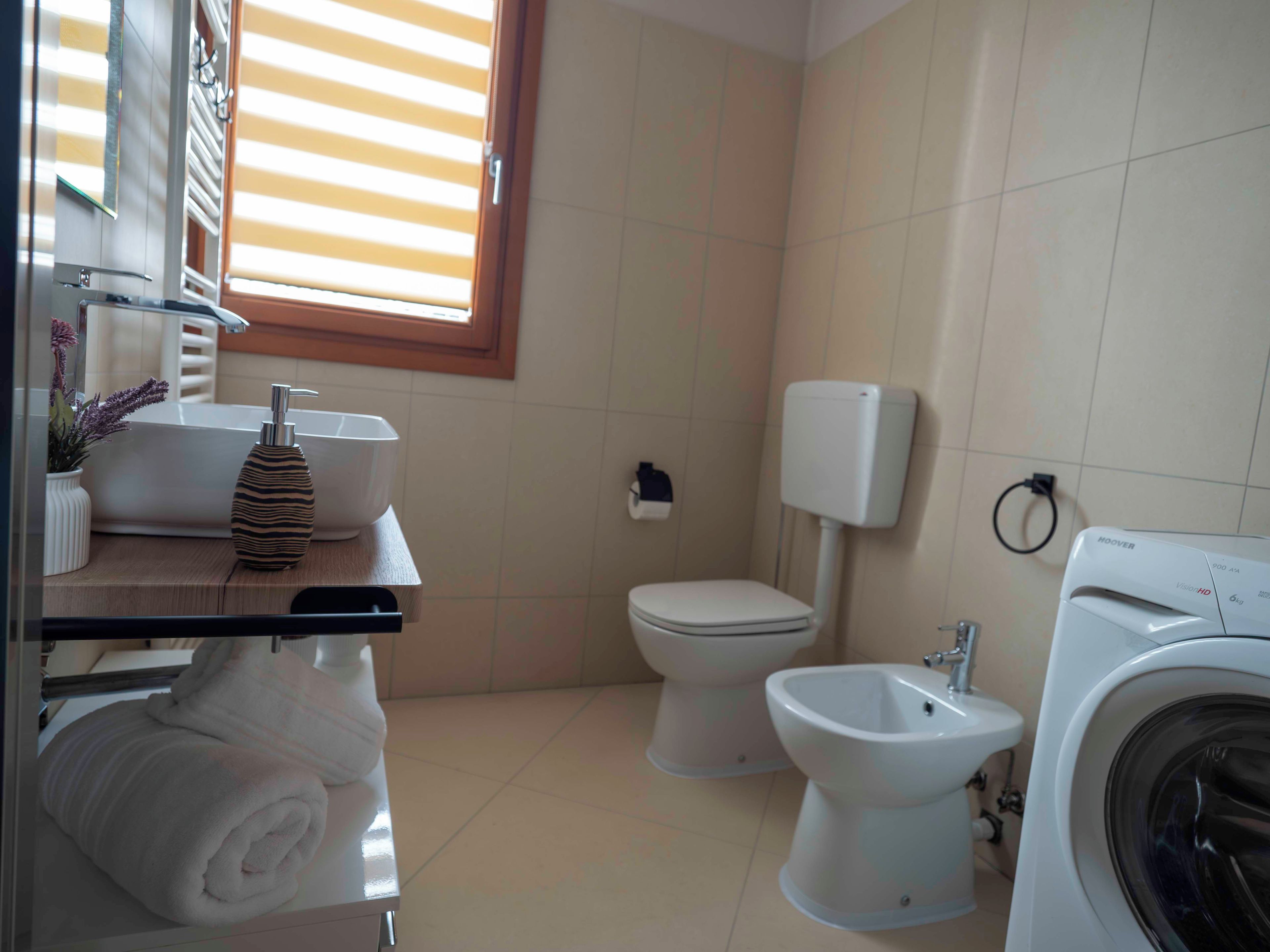 A bathroom with a toilet, bidet, washing machine, and a towel rack with towels.