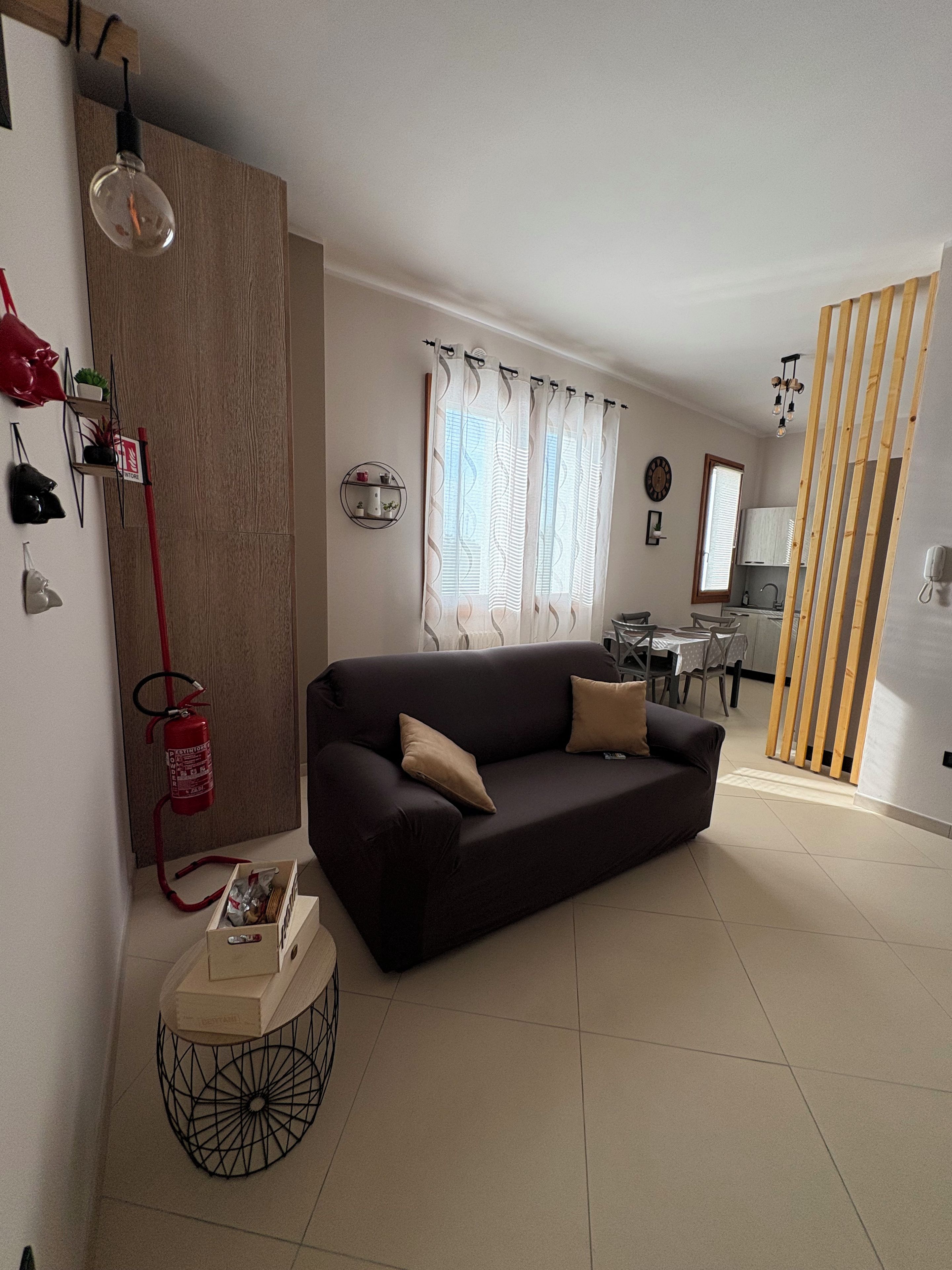 A living room with a dark sofa, a small round coffee table, and a fire extinguisher mounted on the wall.