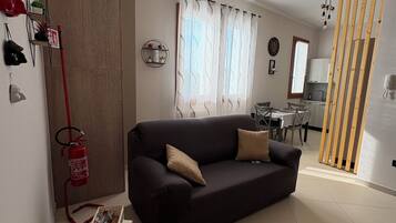A living room with a dark sofa, a small round coffee table, and a fire extinguisher mounted on the wall.