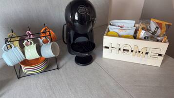 En kaffebryggare, ett ställ för kaffemuggar och en låda för snacks på en bänkskiva.
