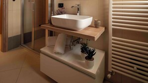 Un baño moderno con un lavamanos grande de color blanco, un espejo, un perchero para toallas y un box de ducha con mampara de vidrio.