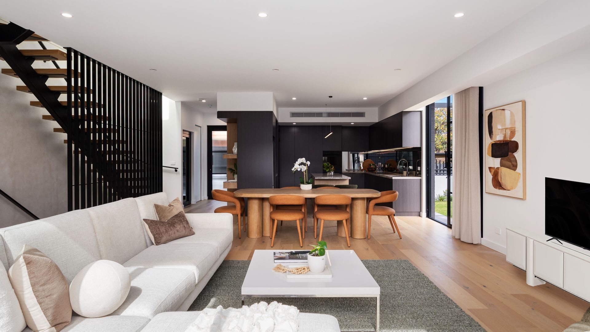A modern living space with a sofa, coffee table, dining area, kitchen, and staircase.