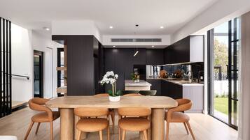 A modern kitchen with a central island, a dining area with a wooden table and chairs, and large windows offering a view of the outdoors.