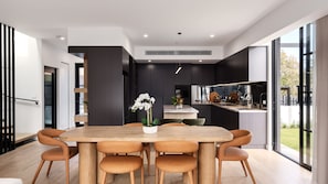 Cozinha moderna com ilha central, área de jantar com mesa e cadeiras de madeira, e grandes janelas com vista para o exterior.