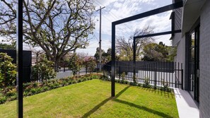 Una propiedad residencial moderna con un césped cuidado, una valla de metal negro y un gran árbol que proporciona sombra.