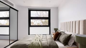 A modern bedroom with a large window, a bed with multiple pillows, and a bedside table with a lamp.