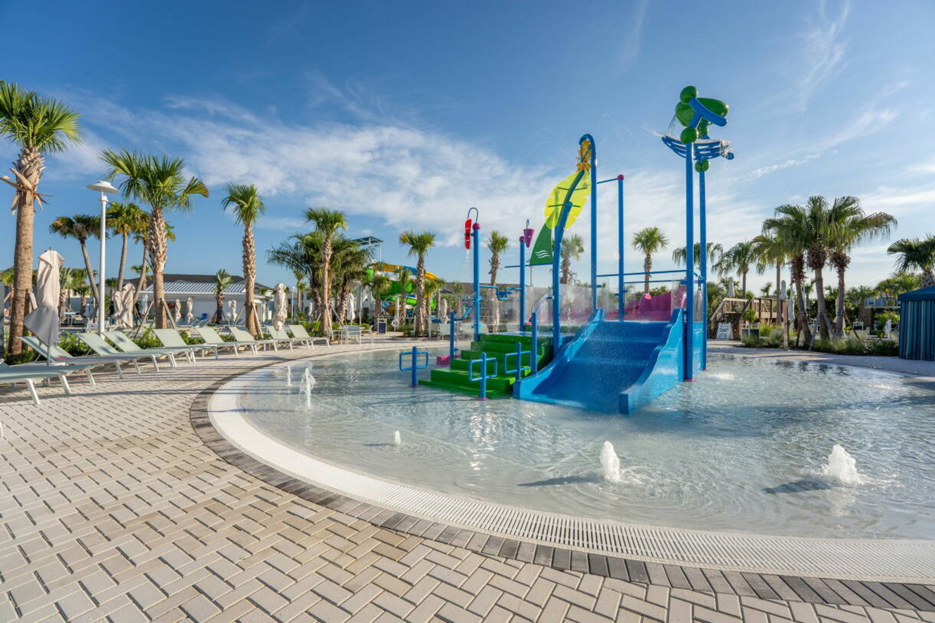 Un parc aquatique avec des toboggans et des fontaines, entouré de palmiers et de chaises longues.