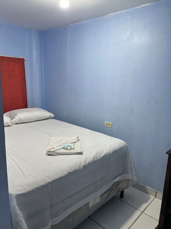 A single bed with a white bedspread and pillows, a folded towel, and two bottles on the bed.