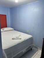 A single bed with a white bedspread and pillows, a folded towel, and two bottles on the bed.