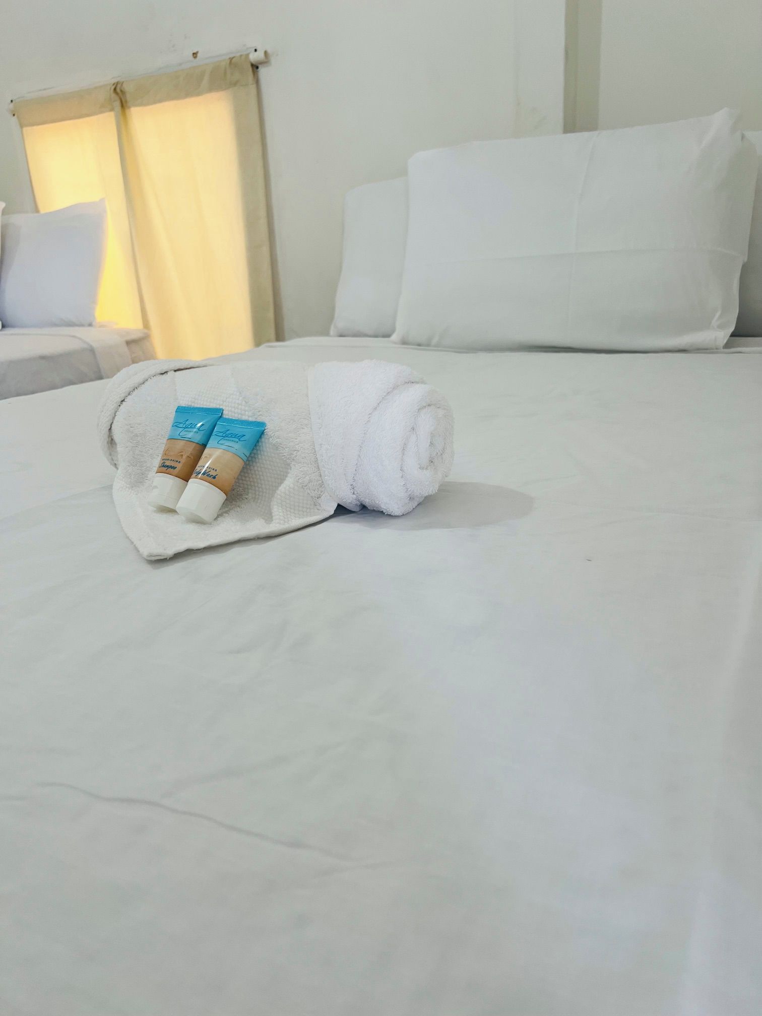 Una cama bien hecha con una toalla blanca enrollada y dos artículos de tocador.