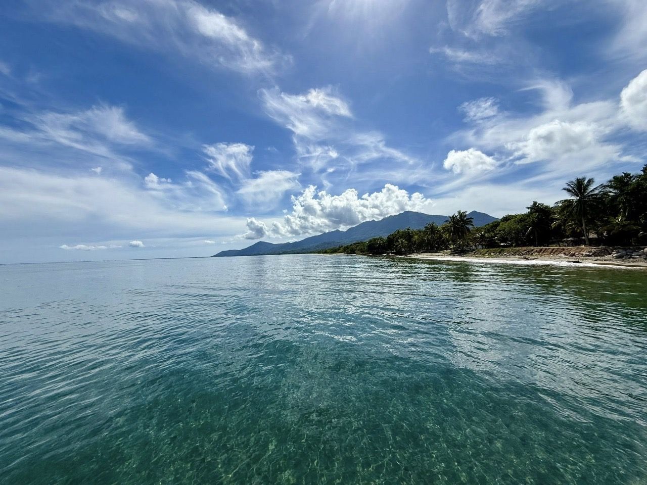 Una vista clara d'una platja amb aigua turquesa, sorra daurada i una muntanya al fons.