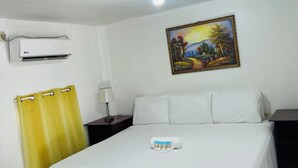 A hotel room with a bed, a painting, an air conditioning unit, and a curtain.
