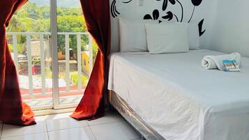 Habitación de hotel con cama, ventana con cortinas rojas, aire acondicionado instalado en la pared y vistas a zonas verdes.