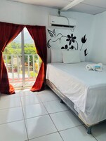 Habitación de hotel con cama, ventana con cortinas rojas, aire acondicionado instalado en la pared y vistas a zonas verdes.