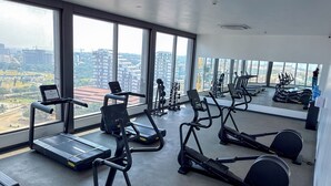 A gym with treadmills, elliptical machines, and weight equipment, with large windows offering a city view. - Luxury 3-Bedroom Condo in Tranquil Accra with Pool and Fitness Room (Accra)