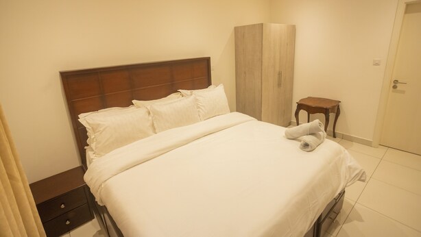 A hotel room with a bed, a wooden headboard, a bedside table, and a wardrobe. - Luxury 3-Bedroom Condo in Tranquil Accra with Pool and Fitness Room (Accra)