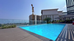A rooftop pool with a clear view of the city skyline, a construction crane, and a modern building in the background. - Luxury 3-Bedroom Condo in Tranquil Accra with Pool and Fitness Room (Accra)