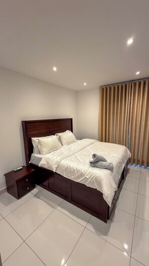 A modern hotel room with a large bed, a nightstand, and a curtain. - Luxury 3-Bedroom Condo in Tranquil Accra with Pool and Fitness Room (Accra)