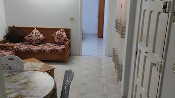 A room with a sofa, a table with chairs, a door, and a hallway leading to another room.