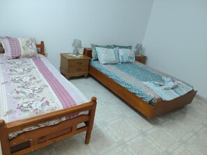 A bedroom with two wooden beds, each with floral bedding and pillows. There are bedside tables with lamps and a small drawer. - Studio Amine  (Mahdia)