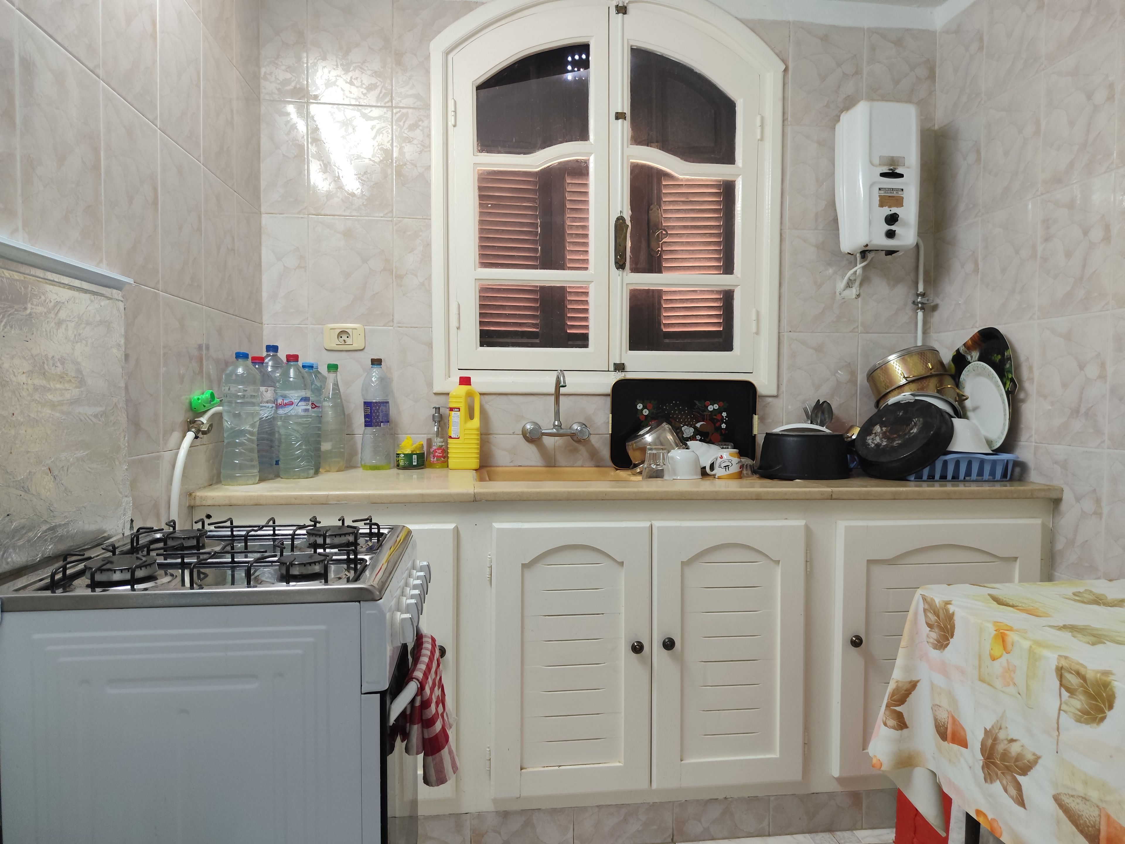 A kitchen with a gas stove, a sink, and cabinets. There are various kitchen items on the counter.