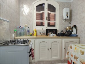 Una cocina con estufa a gas, un lavamanos y alacenas. Hay varios utensilios de cocina sobre la encimera.