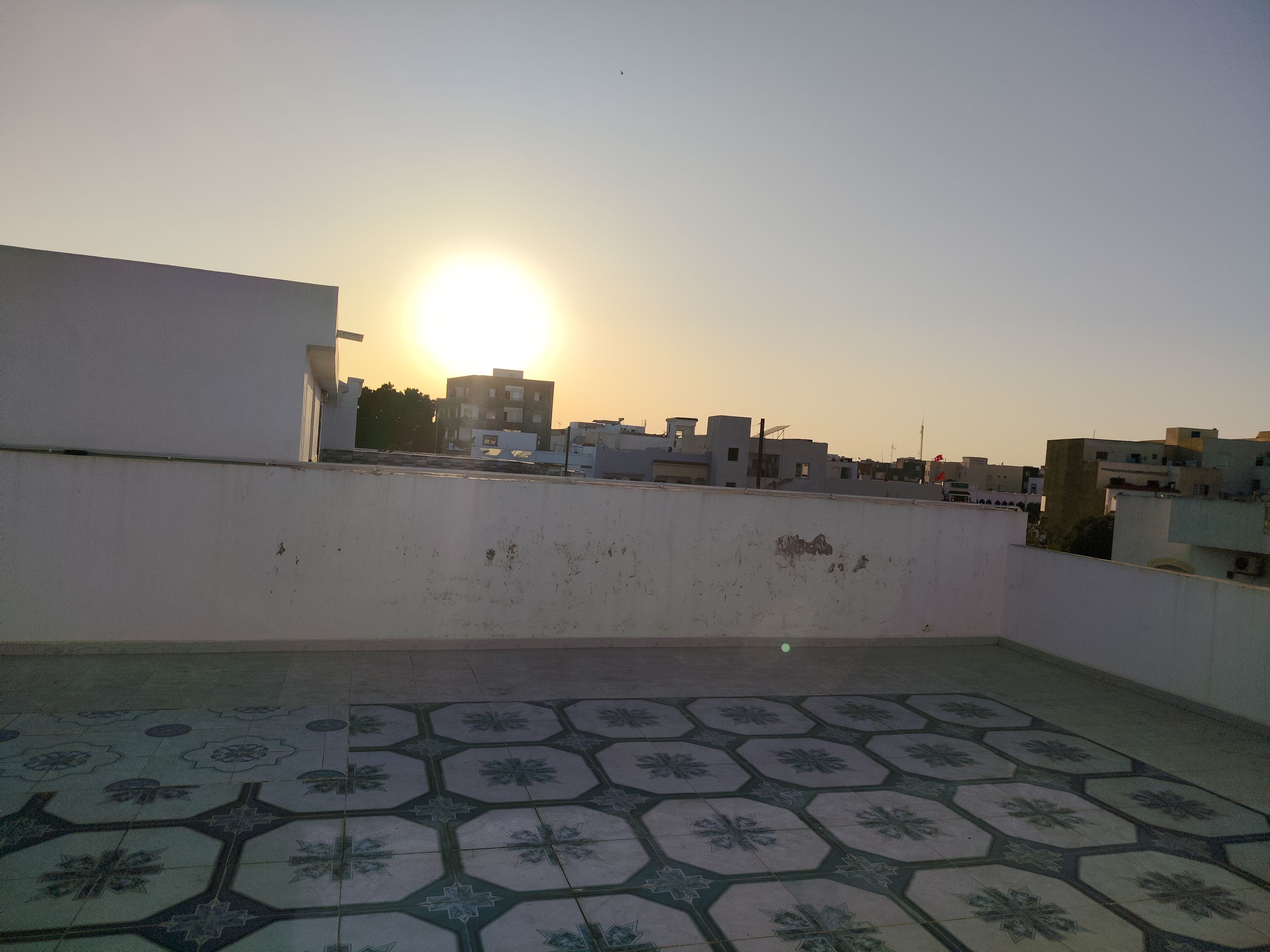 Une terrasse sur le toit, dotée d’un sol à motifs et offrant une vue sur les bâtiments au loin, au coucher du soleil.