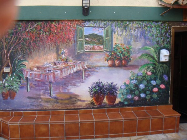 A mural with a table set for dining, surrounded by potted plants and flowers.