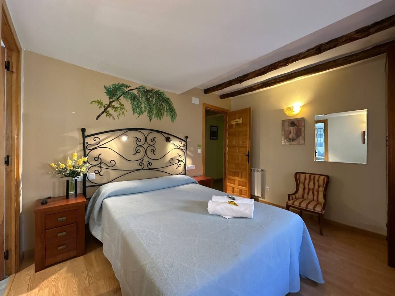 Un dormitorio con cama, mesita de noche, silla, puerta de madera y lámpara fijada a la pared.