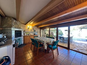 A kitchen with a stone wall, wooden beams, a dining table with chairs, and a view of the outside patio.