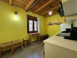 A room with a wooden ceiling, a window with curtains, a small table, a bench, and a coffee machine.
