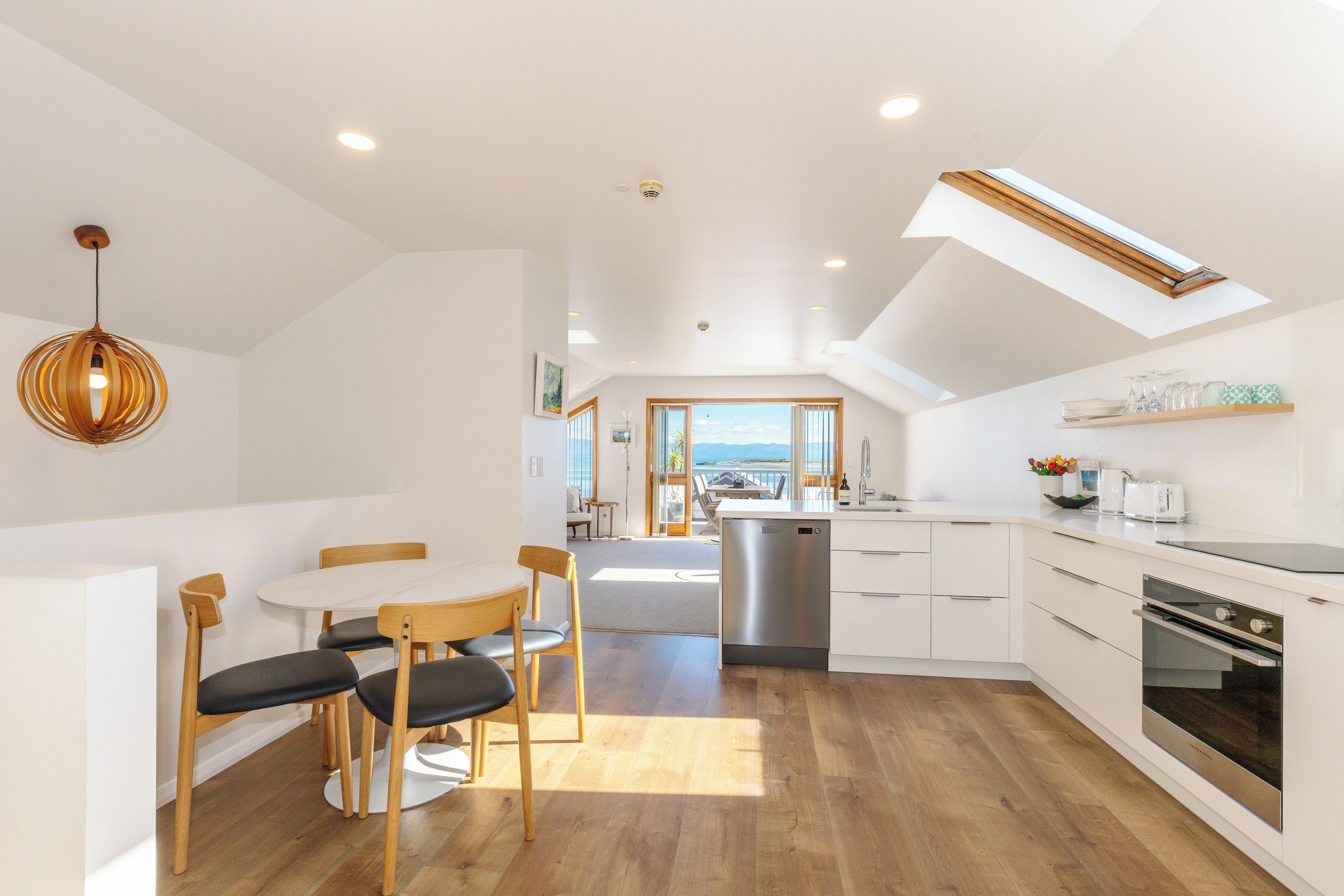A modern kitchen with a central island, wooden flooring, and a dining area with a round table and chairs.