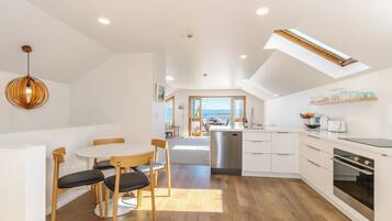 A modern kitchen with a central island, wooden flooring, and a dining area with a round table and chairs.